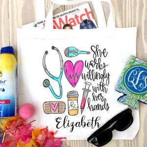 May include: White tote bag featuring a pink heart, stethoscope, syringe, bandage, and pill bottle. The text "She works willingly with her hands Elizabeth" is printed on the bag.