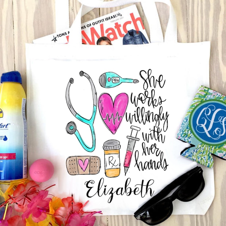 May include: White tote bag featuring a pink heart, stethoscope, syringe, bandage, and pill bottle. The text "She works willingly with her hands Elizabeth" is printed on the bag.