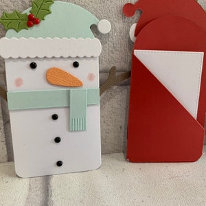Puede incluir: Una colecci&oacute;n de dise&ntilde;os de tarjetas navide&ntilde;as hechas a mano. Las tarjetas presentan un mu&ntilde;eco de nieve con un gorro y bufanda verde menta, una tarjeta de Pap&aacute; Noel y una tarjeta de ping&uuml;ino. El mu&ntilde;eco de nieve tiene una nariz de zanahoria naranja y ojos de bot&oacute;n negros.