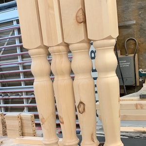 May include: Four unfinished wooden table legs with a turned design. The legs are made of light-colored wood and have a smooth finish.