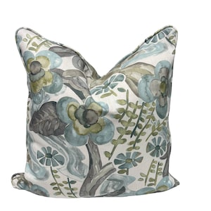 May include: A decorative throw pillow with a floral pattern in shades of blue, green, and gray. The pillow has a white background and features a watercolor-like design.