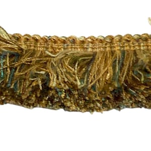 Puede incluir: Primer plano de un ribete de flecos decorativos. El ribete presenta un diseño texturizado con una combinación de colores oro, marrón y turquesa. Los flecos están hechos de múltiples hebras, creando un efecto en capas. Este ribete es adecuado para proyectos de manualidades y costura.
