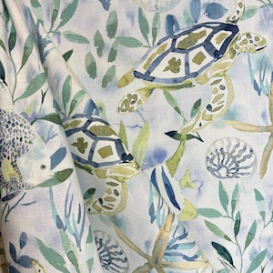 May include: A watercolor-style fabric featuring a repeating pattern of sea turtles, seashells, and seaweed in shades of blue, green, and yellow on a white background.