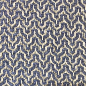 May include: A close-up of a woven fabric with a blue and beige geometric pattern. The fabric has a textured surface and a subtle sheen.