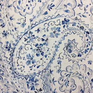 May include: White fabric with a blue and gray paisley pattern. The pattern features intricate swirls and floral designs.