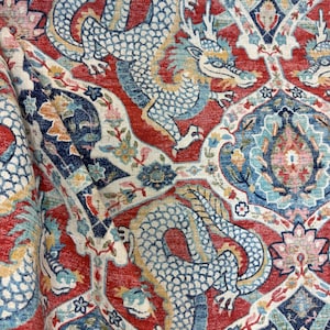 May include: Close-up of a red, blue, and cream-colored fabric with a repeating pattern of dragons and floral motifs. The dragons are light blue with yellow accents, set against a red background with intricate details.