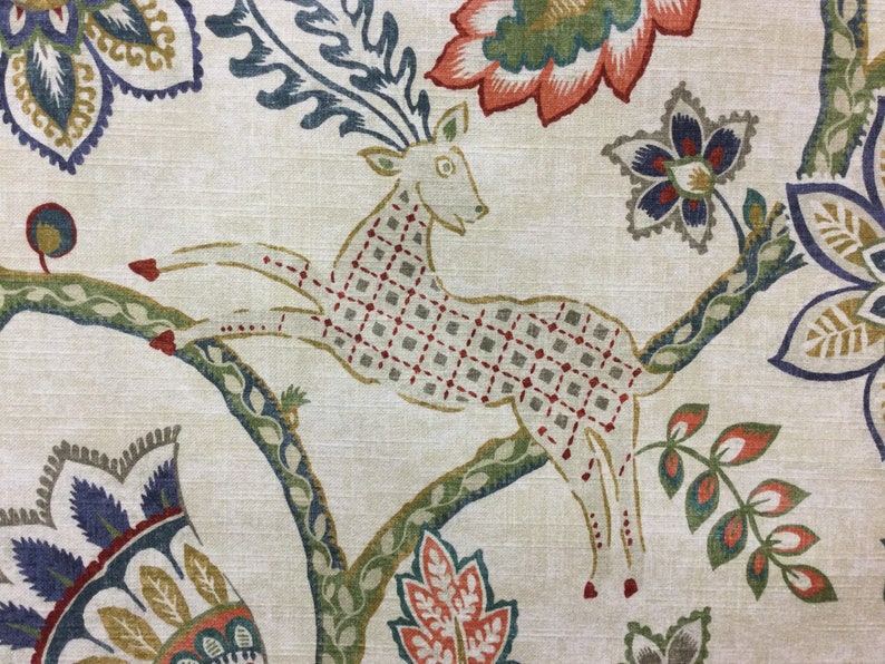 May include: A beige fabric featuring a repeating pattern of a leaping deer with a red and grey grid design on its body. The deer is surrounded by large, stylized floral motifs in shades of orange, blue, green, and yellow, set against a textured background.