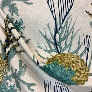 May include: A beige fabric with a repeating pattern of blue, green, and gold sea life. The pattern features coral, seaweed, and seahorses.