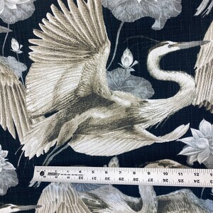 May include: Black fabric with a repeating pattern of white and gray cranes and lotus flowers. The cranes are depicted in flight with their wings spread wide. The lotus flowers are stylized and have a delicate appearance.