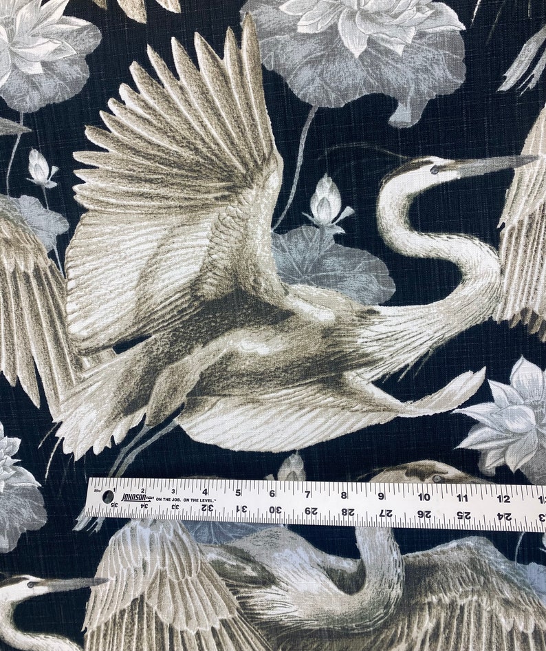 May include: Black fabric with a repeating pattern of white and gray cranes and lotus flowers. The cranes are depicted in flight with their wings spread wide. The lotus flowers are stylized and have a delicate appearance.