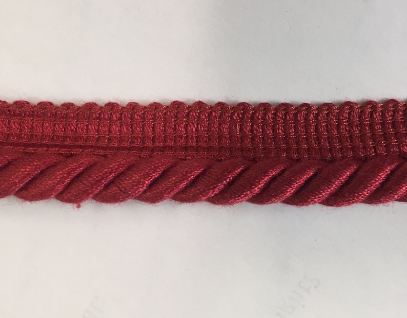 May include: Red braided trim with a woven top edge. This trim is perfect for adding a touch of elegance to any project.
