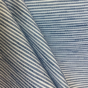 May include: Close-up of a blue and white striped fabric with a textured weave. The fabric is folded in half, creating a diagonal line.