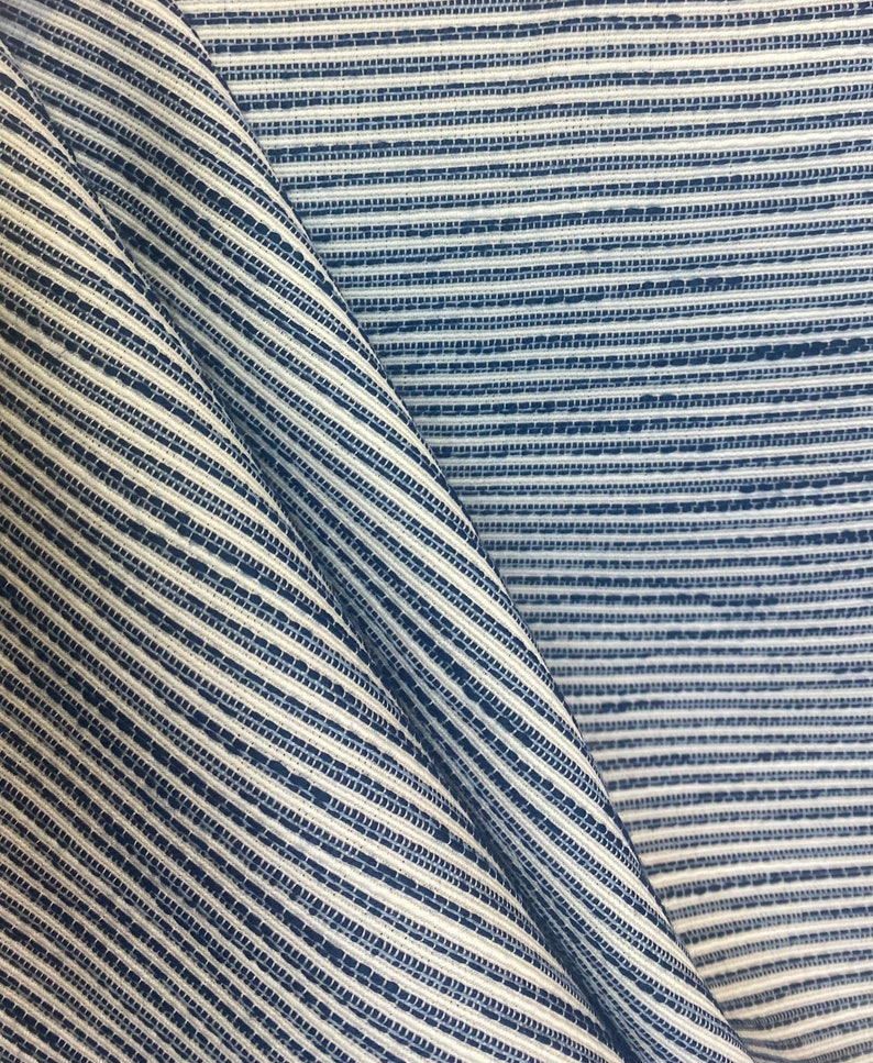 May include: Close-up of a blue and white striped fabric with a textured weave. The fabric is folded in half, creating a diagonal line.