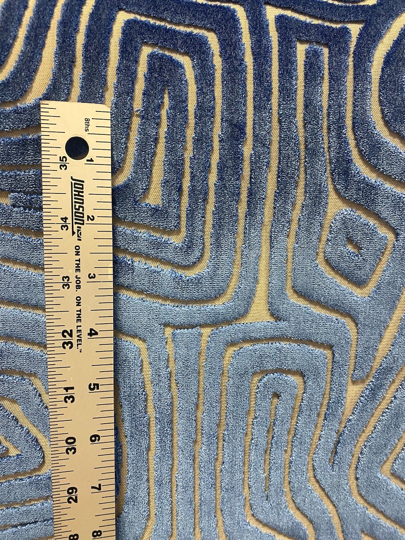 May include: Close-up of a blue and beige fabric with a geometric pattern. The fabric has a textured, velvety feel. A ruler is visible in the image, showing a measurement of 35 inches.