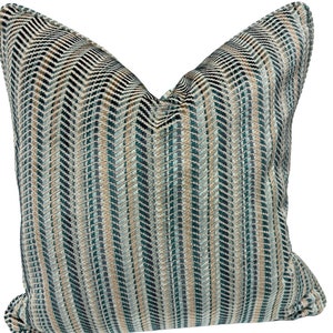May include: A decorative throw pillow with a geometric pattern in shades of blue, green, and beige. The pillow has a chevron pattern with vertical stripes.