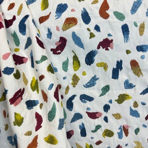 May include: White fabric with a repeating pattern of colorful abstract shapes. The shapes are embroidered in various shades of blue, green, yellow, orange, red, and pink.