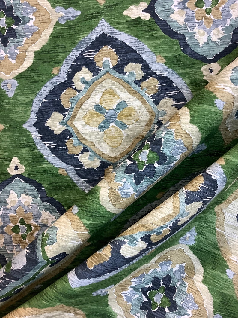 May include: Green fabric with a blue and beige ikat pattern. The fabric has a soft, textured feel and is perfect for upholstery or drapery.