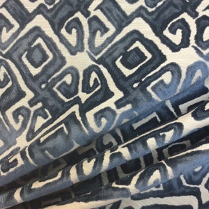 May include: Close-up of a fabric with a repeating geometric pattern in shades of blue and white. The design features stylized square shapes with curved interior elements, creating a textured appearance. The fabric is folded, showing depth and dimension.