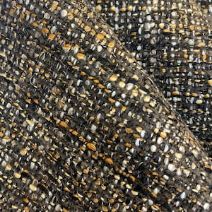 May include: Close-up of a textured fabric with a black, white, and gold color scheme. The fabric has a woven appearance with a subtle diagonal pattern.