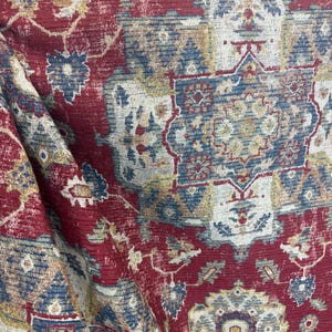 May include: Close-up of a red, blue, and gold patterned rug. The rug features a traditional design with floral and geometric motifs. The colours are rich and the texture appears soft.