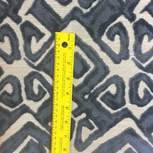 May include: Close-up of a fabric with a repeating geometric pattern in shades of blue-gray on a light beige background. A yellow ruler is placed vertically, showing measurements in inches and centimeters.