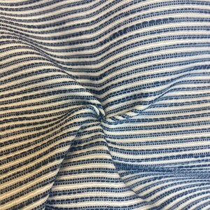 May include: Close-up of a blue and white striped fabric with a textured weave. The fabric is folded and wrinkled, showing the texture of the weave.