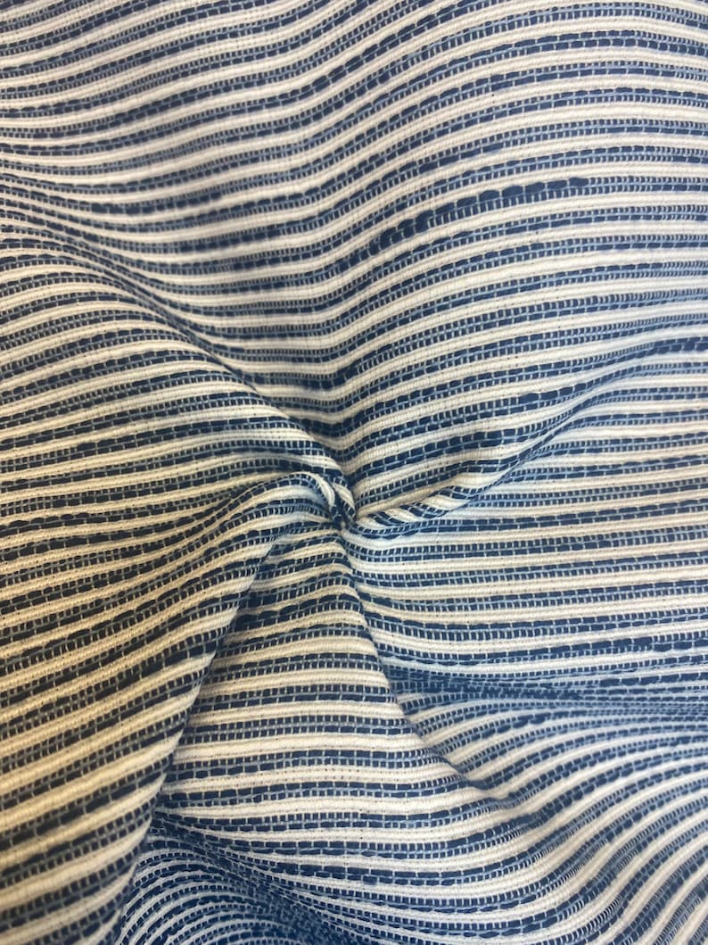 May include: Close-up of a blue and white striped fabric with a textured weave. The fabric is folded and wrinkled, showing the texture of the weave.