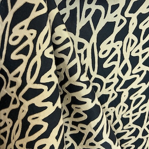 May include: Black fabric with a white abstract pattern of lines and swirls. The fabric is folded in half, showing the pattern on both sides.