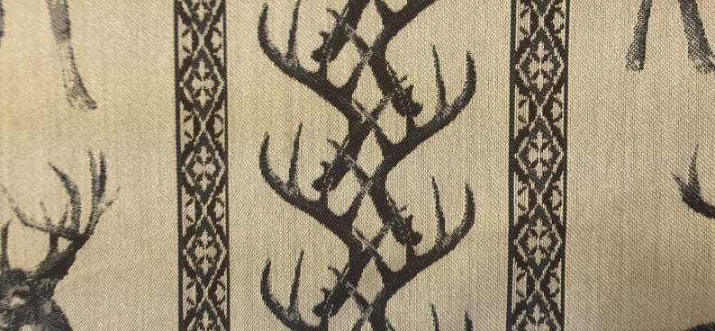 May include: Beige fabric with a repeating pattern of black stylized deer antlers. The antlers are arranged in a criss-cross pattern.
