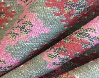May include: Close-up of a folded fabric with a repeating pattern of pink, red, and grey flowers. The fabric has a woven texture.