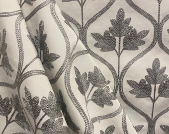 May include: White fabric with a repeating pattern of gray embroidered floral designs. The design features stylized leaves and stems.