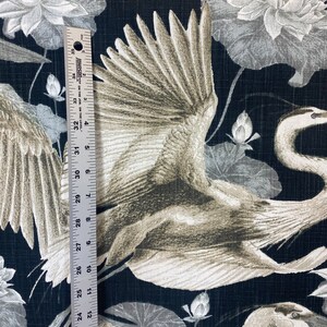 May include: Black fabric with a white and gray crane pattern. The crane is flying with its wings spread. The background is a dark black with a subtle texture. The fabric has a repeating pattern of cranes and lotus flowers.