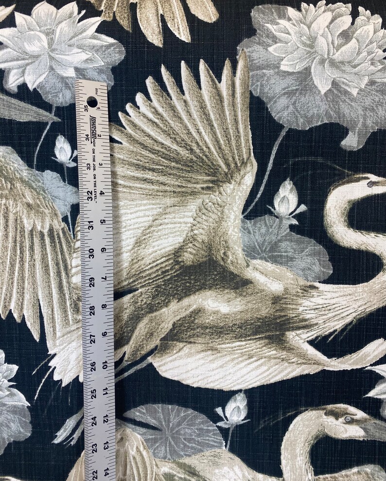 May include: Black fabric with a white and gray crane pattern. The crane is flying with its wings spread. The background is a dark black with a subtle texture. The fabric has a repeating pattern of cranes and lotus flowers.