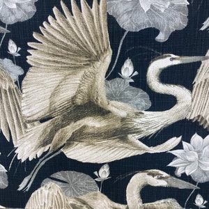 May include: A black fabric with a repeating pattern of white and gray cranes and lotus flowers. The cranes are flying with their wings spread out. The lotus flowers are in bloom.