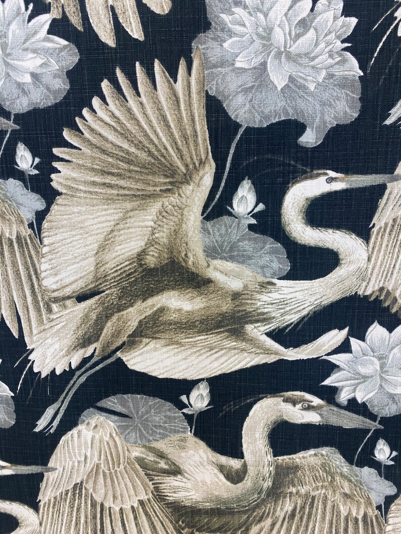 May include: A black fabric with a repeating pattern of white and gray cranes and lotus flowers. The cranes are flying with their wings spread out. The lotus flowers are in bloom.