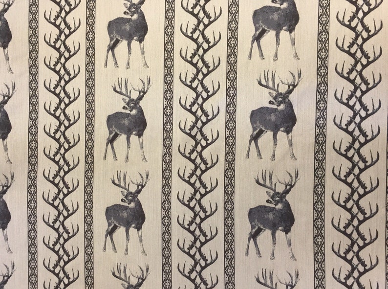 May include: A beige fabric with a repeating pattern of black deer and stylized antlers. The deer are facing right and have large antlers. The antlers are stylized and look like a series of connected branches.