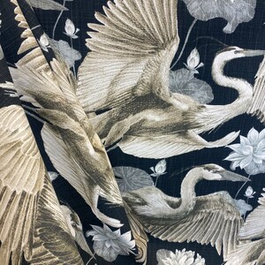 May include: Black fabric with a repeating pattern of white and gray herons and lotus flowers. The herons are depicted with their wings spread, and the lotus flowers are in full bloom.