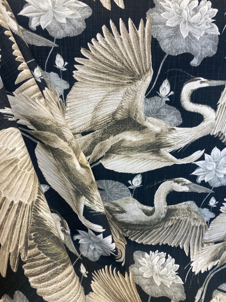 May include: Black fabric with a repeating pattern of white and gray herons and lotus flowers. The herons are depicted with their wings spread, and the lotus flowers are in full bloom.