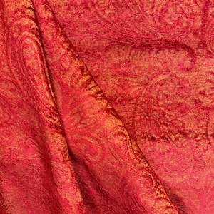 May include: Red fabric with a gold metallic pattern. The fabric is textured and has a subtle sheen.