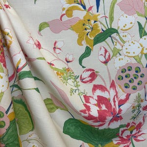 May include: Floral fabric featuring a cream background with a repeating pattern of colorful flowers and foliage. The design includes yellow lilies, pink lotus flowers, and green leaves. The fabric is folded, showing the texture and drape.