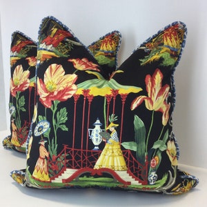 May include: Two black pillow covers with a floral design featuring red, yellow, and green flowers, a red bridge, and a woman in a yellow dress. The pillow covers have a blue scalloped edge.