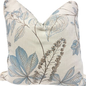 May include: A cream-colored throw pillow with a blue and brown leaf pattern. The pillow has a subtle texture and a slightly frayed edge.