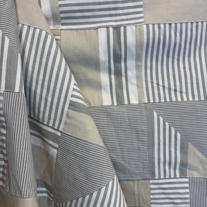 May include: A patchwork fabric featuring a range of grey and white striped patterns. The fabric is folded and draped, showcasing the various designs.