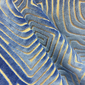 May include: Blue and beige patterned fabric with a textured, raised design. The fabric has a geometric pattern of overlapping lines and squares.