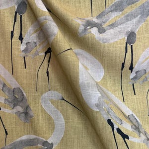 Pode incluir: Close-up de tecido com um padr&atilde;o repetido de gar&ccedil;as brancas e cinzentas sobre um fundo amarelo. As gar&ccedil;as t&ecirc;m pesco&ccedil;os e pernas longas, com detalhes em preto. O tecido tem uma apar&ecirc;ncia texturizada.