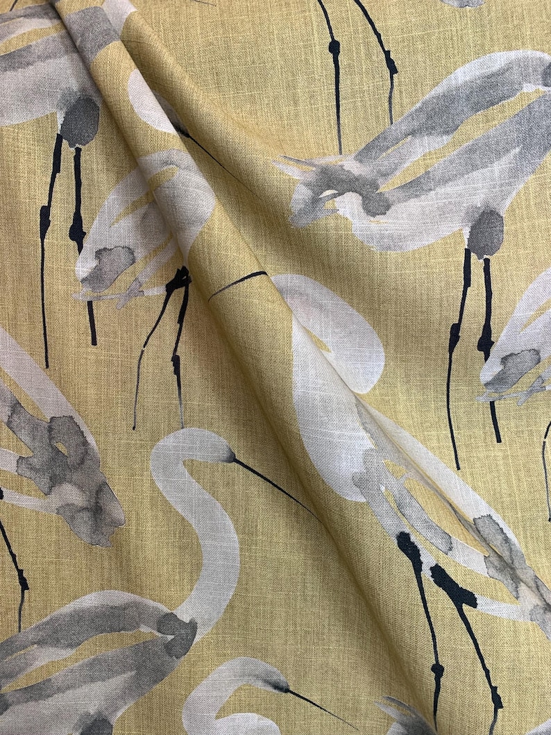 Pode incluir: Close-up de tecido com um padr&atilde;o repetido de gar&ccedil;as brancas e cinzentas sobre um fundo amarelo. As gar&ccedil;as t&ecirc;m pesco&ccedil;os e pernas longas, com detalhes em preto. O tecido tem uma apar&ecirc;ncia texturizada.