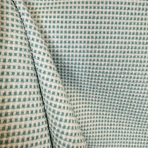 May include: A close-up of a fabric with a checkered pattern in shades of light grey and teal.