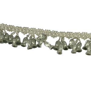 May include: Silver-colored fringe trim with a woven top edge and bell-shaped drops. The trim is a metallic silver color and is against a white background. The fringe is likely used for decorative purposes on clothing or home decor items.