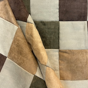 May include: A patchwork fabric with squares of brown, tan, and gray. The fabric is folded and has a soft, fuzzy texture.