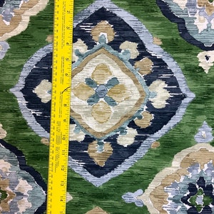 May include: Green, blue, and beige fabric with a repeating pattern of stylized flowers and geometric shapes. The fabric is measured with a yellow ruler.